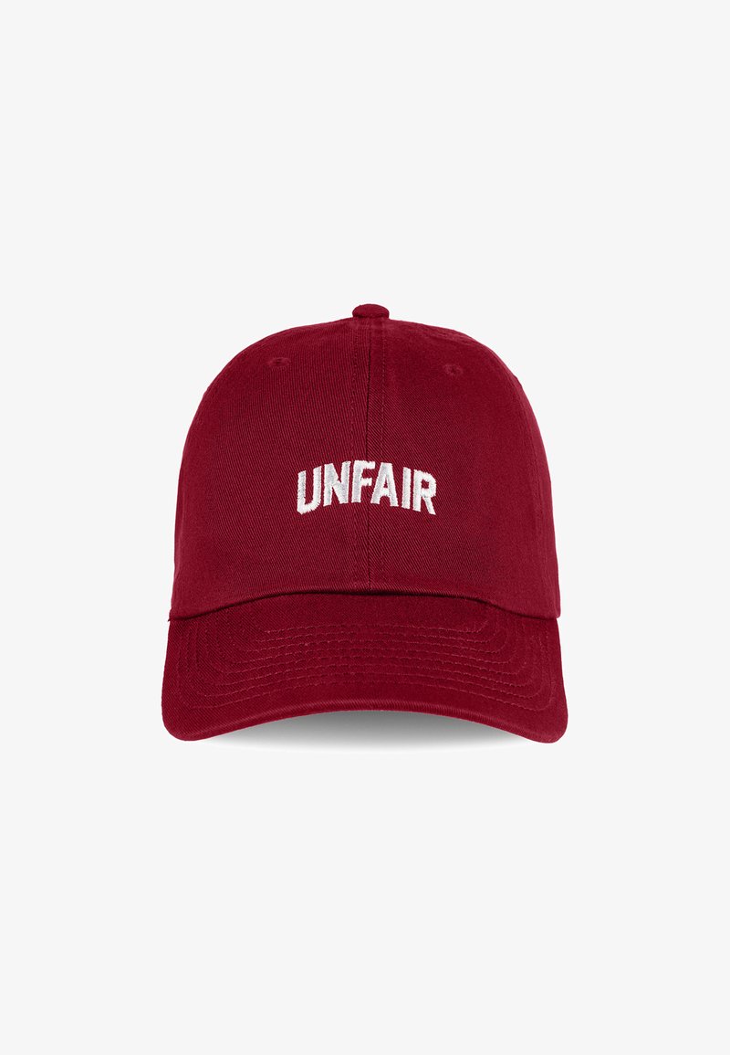 Red cotton cap with a curved visor and adjustable strap. Features "UNFAIR" embroidered in white across the front. Textured fabric.