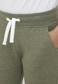 Olijfgroene joggingsbroek met een zachte textuur, voorzien van een witte trekkoord en zijzakken, ontworpen voor comfort en casual gebruik.