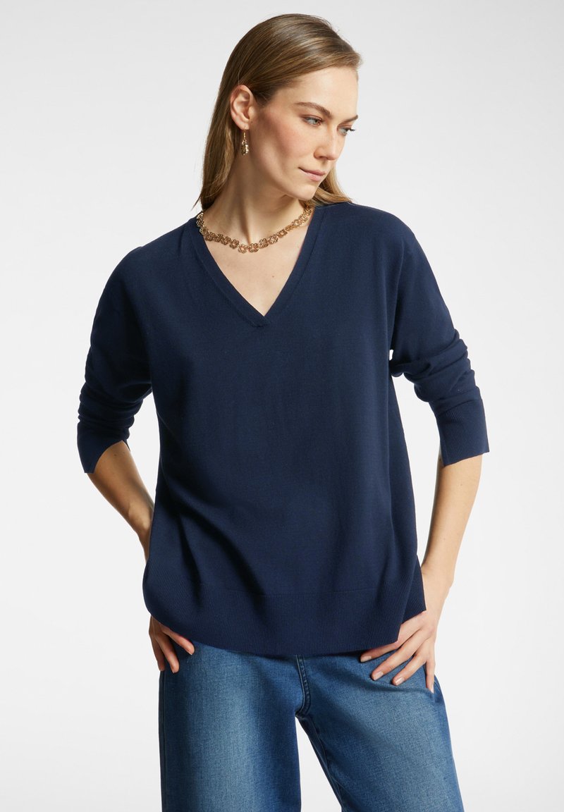 Jersey de cuello en V azul marino hecho de material suave, con mangas largas y un corte relajado. Combinado con unos vaqueros de pierna ancha azul claro.