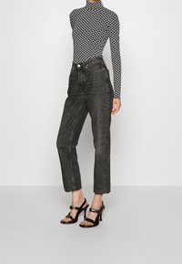 Maglione a collo alto a righe bianche e nere, jeans scuri a vita alta, e sandali neri con tacco alto, che mettono in risalto una silhouette aderente.