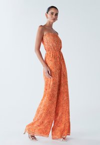 Oranje strapless jumpsuit met bloemmotief, geplooide bovenkant, getailleerde taille en broekspijpen met wijde pijpen. Doorzichtig, lichtgewicht stof.