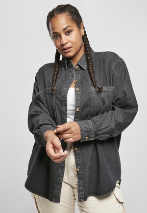 Black denim button-up shirt with long sleeves, front pocket, and rounded hem. Model wears a white tank underneath.