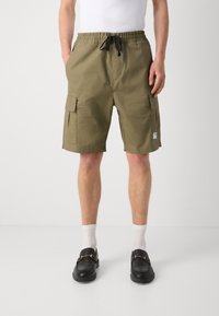 Shorts kaki cu talie elastică, cu buzunare frontale și două buzunare laterale pentru cargo. Purtați cu șosete albe și loaferi negri.
