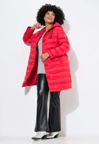 Röd puffjacka med huva, med horisontella sömmar och tryckknappar. Matchad med svarta utsvängda byxor och silverfärgade klackskor med blockformat häl.