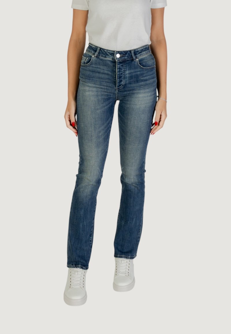 Vaqueros de mezclilla azul con una cintura ajustada, pierna recta, cinco bolsillos y un leve desgastado. Combinados con zapatillas blancas y una camiseta gris.