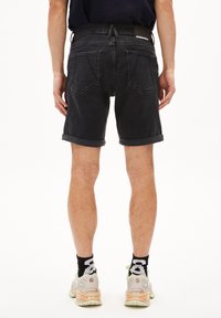 Zwarte denim shorts met opgerolde boorden, een vijf-pocket ontwerp, en een logo op de tailleband, gecombineerd met lichte sneakers en zwarte sokken.