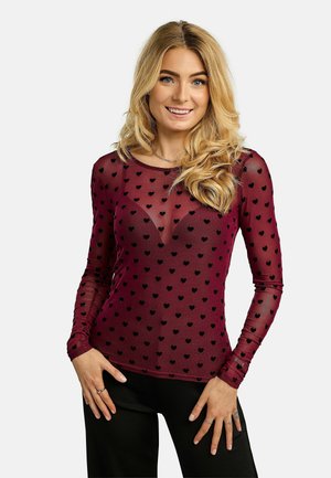 Haut en bordeaux transparent à manches longues, orné de petits motifs de cœurs noirs, col arrondi et texture lisse. Associé à un pantalon noir.