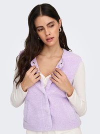 Chaleco de forro polar color púrpura claro con superficie texturizada, cierre frontal de botones a presión y sin mangas. Llevado sobre una camiseta blanca de manga larga.