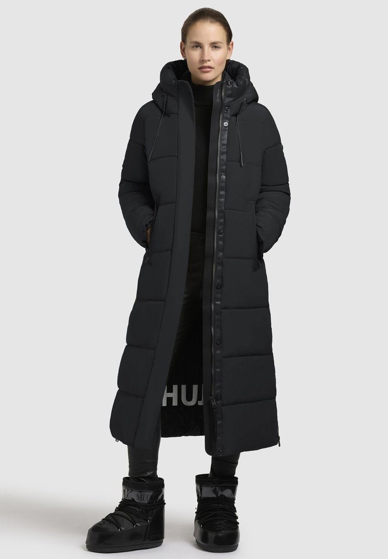 Lang sort dunfrakke med hætte, med et quiltet design, frontknapper og sidelommer. Glat tekstur med lynlås lukning.