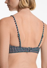 Soutien-gorge avec bretelles fines réglables, présentant un design tissé à motifs en bleu profond, bordeaux et blanc. Fermeture à crochet à l'arrière visible.