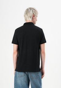 Polo shirt noir à manches courtes avec un col classique et une texture subtile, vu de dos, associé à un jean en denim bleu clair.