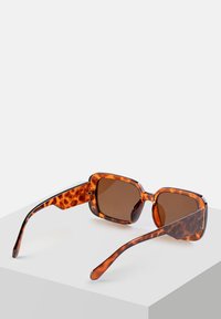 Okulary przeciwsłoneczne w kolorze żółwia z kwadratowymi oprawkami, brązowymi soczewkami i gładką plastikową teksturą. Posiadają grube ramiona z wzorzystym designem.