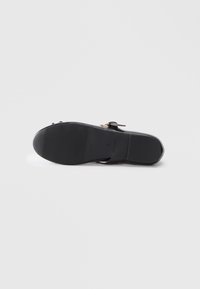 Zwarte sandaal met een platte zool, een gestructureerde rubberen buitenzool en gouden hardware. Beschikt over een verstelbare enkelband en een minimalistisch ontwerp.