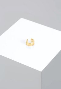 Inel cu tonuri de aur, cu o finisare texturată, având un design cu bandă deschisă și o suprafață ușor ciocănită. Poziționat pe un pedestal alb.