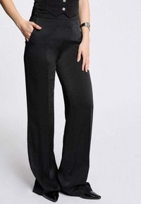Pantalons larges noirs en tissu lisse, avec des poches latérales, une taille haute et une silhouette élégante.