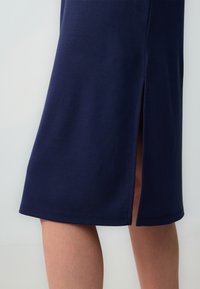 Gonna blu navy al ginocchio, realizzata in tessuto liscio, presenta una fessura laterale e un orlo dritto. La cucitura è ordinata, senza accenti hardware visibili.