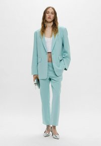 Blazer tagliato verde menta e pantaloni coordinati in un tessuto morbido, abbinati a un crop top bianco e tacchi a punta argentati.