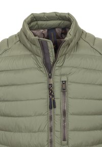 Padded olivgrüne Jacke mit einem Reißverschluss vorne, hohem Kragen und zwei seitlichen Reißverschlüssen. Sie hat eine vertikale Stepptextur und marineblaue Akzente.