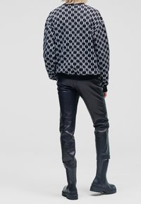 Schwarze Bomberjacke mit weißem geometrischem Muster, kombiniert mit eng anliegenden schwarzen Lederhosen und Stiefeletten, die ein schlankes, modernes Design präsentieren.