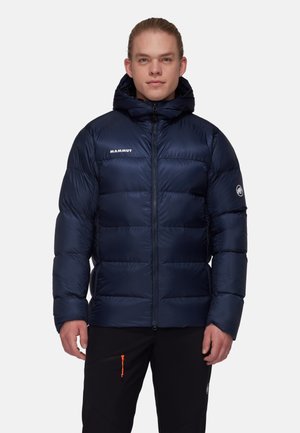 Navy blue puffer jacket with a hood, featuring stitched segments for insulation, a front zipper, and a logo on the chest and sleeve.