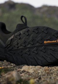Suola di scarpa outdoor nera con battistrada profondo e marchio Continental che poggia su terreno roccioso all'aperto.