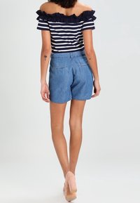Modré denimové šortky s uvolněným střihem, rozšířeným lemem a zadními kapsami. V kombinaci s námořnickým pruhovaným topem bez ramínek s volány.