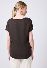 Hnědý krátký rukáv top s kulatým výstřihem a uvolněným střihem. Vyrobeno z měkkého materiálu, s jemnou texturou a volně drapovaným designem vzadu.