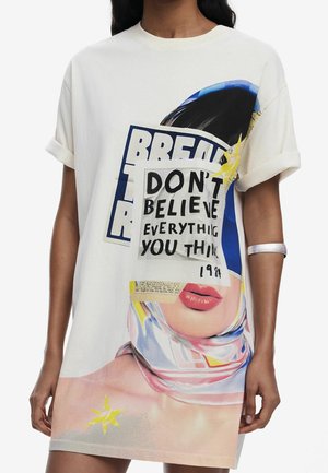 Kvinde iført en hvid kjole med et grafikprint af et ansigt, tørklæde og tekst, der lyder "TRUST IKKE ALT, HVAD DU TÆNKER 1981."
