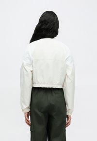 Κοντό μπουφάν bomber σε κρεμ και λευκό χρώμα, με ελαστικά μανίκια και τελείωμα, σε συνδυασμό με cargo παντελόνι σε σκούρο πράσινο χρώμα. Ομαλή υφή υλικού.