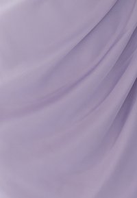 Lavendli värvi kangas pehme tekstuuriga, millel on napp drapeering ja pehmed voolavad lained. Pinnalt peegeldub kerge valgus.