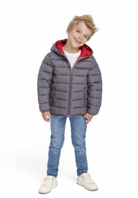 Gray padded jacket with a red hood and lining, featuring a front zipper and side pockets, worn with blue jeans and white sneakers.