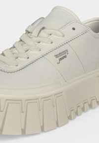 Baskets blanches avec semelle épaisse, lacets épais, couture en zigzag, et petit logo métallique "tommy jeans" sur le panneau latéral.
