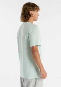 Camiseta de manga corta en verde menta claro hecha de una tela suave. Diseño de cuello redondo, corte relajado y textura suave sin patrones visibles.