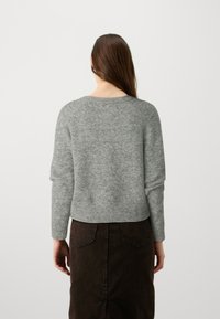 Pull gris tricoté à manches longues et col rond, présentant une texture subtile. Associé à une jupe marron foncé.