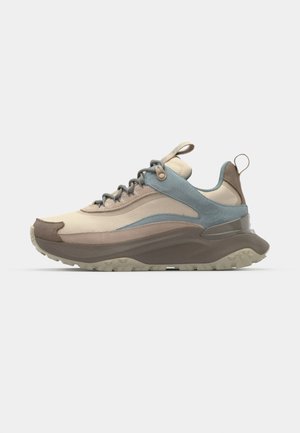 Sneaker mit einem beige-farbenen Mesh-Obermaterial, braunen und blauen Akzenten, strukturierten Einsätzen, einer dicken, grauen Gummisohle und einem Zugband an der Ferse.