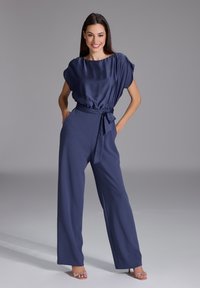 Combinaison en satin bleu marine avec un décolleté large drapé et des manches courtes. Dotée d'une taille cintrée avec un lien assorti et des pantalons à jambes larges.