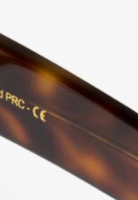 Monture de lunettes de soleil en acétate écaille de tortue avec une texture lisse, comportant des lettres dorées et des détails de logo sur la branche.