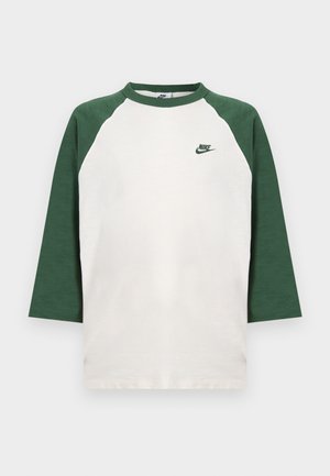 White shirt with green raglan sleeves and collar, featuring a small green Nike logo on the left chest.
