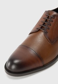 Scarpa in pelle marrone con punta rotonda, caratterizzata da un corpo testurizzato e una punta liscia. Chiusura con lacci e dettagli in contrasto.