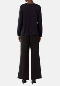 Granatowa bluzka z długim rękawem i kwadratowym dekoltem, zestawiona z czarnymi spodniami o szerokich nogawkach, noszona z czarnymi szpilkami. Gładka faktura materiału.