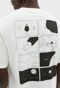 Camiseta blanca con un diseño gráfico negro en la parte posterior, que representa seis paneles al estilo de cómic con ilustraciones minimalistas y elementos abstractos.