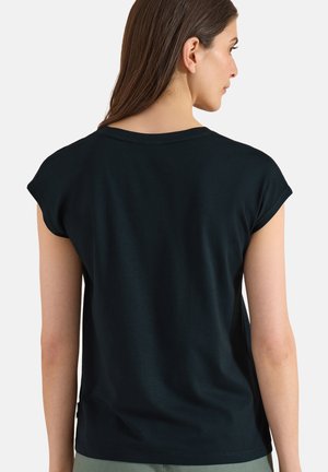 Femme aux longs cheveux bruns portant un t-shirt noir uni à manches courtes, vue de dos sur un fond blanc.