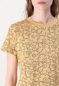 Yellow cotton T-shirt featuring a repeated black floral pattern. Short sleeves and a round neckline. Smooth texture with a relaxed fit.