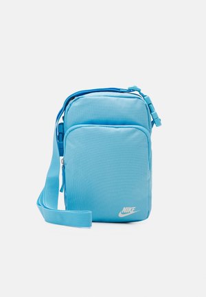 Hellblaue Nike Crossbody-Tasche mit verstellbarem Riemen, vorderer Reißverschlusstasche und weißem Nike-Logo auf einfarbigem Hintergrund.