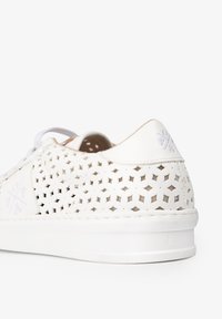 Zapatilla blanca perforada con parte superior texturizada, cordones en contraste y suela lisa. Presenta un sutil detalle del logo cerca del talón.