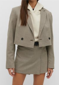 Cropped check-patterned blazer in beige and black, with double buttons. Paired with a cream hoodie and a matching mini skirt.
