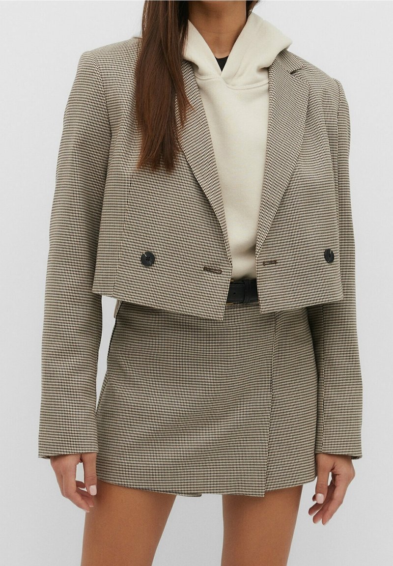 Cropped check-patterned blazer in beige and black, with double buttons. Paired with a cream hoodie and a matching mini skirt.