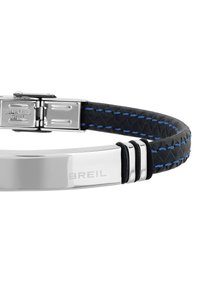 Armbandet i rostfritt stål har ett svart texturerat band med blå sömmar och en glänsande metallplatta graverad med "BREIL".