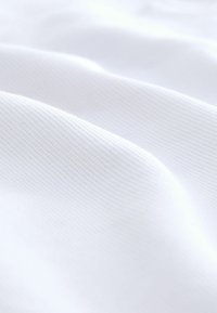 Tejido blanco texturizado con sutil ribete, presentando suaves y lisas ondulaciones. El material parece ligero y uniforme en color.