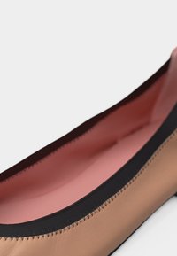 Μπαλαρίνα από δέρμα καμηλοπάρδαλης με μαύρο ελαστικό περίγραμμα και ροζ εσωτερική επένδυση, απεικονίζεται σε κοντινή διαγώνια όψη.